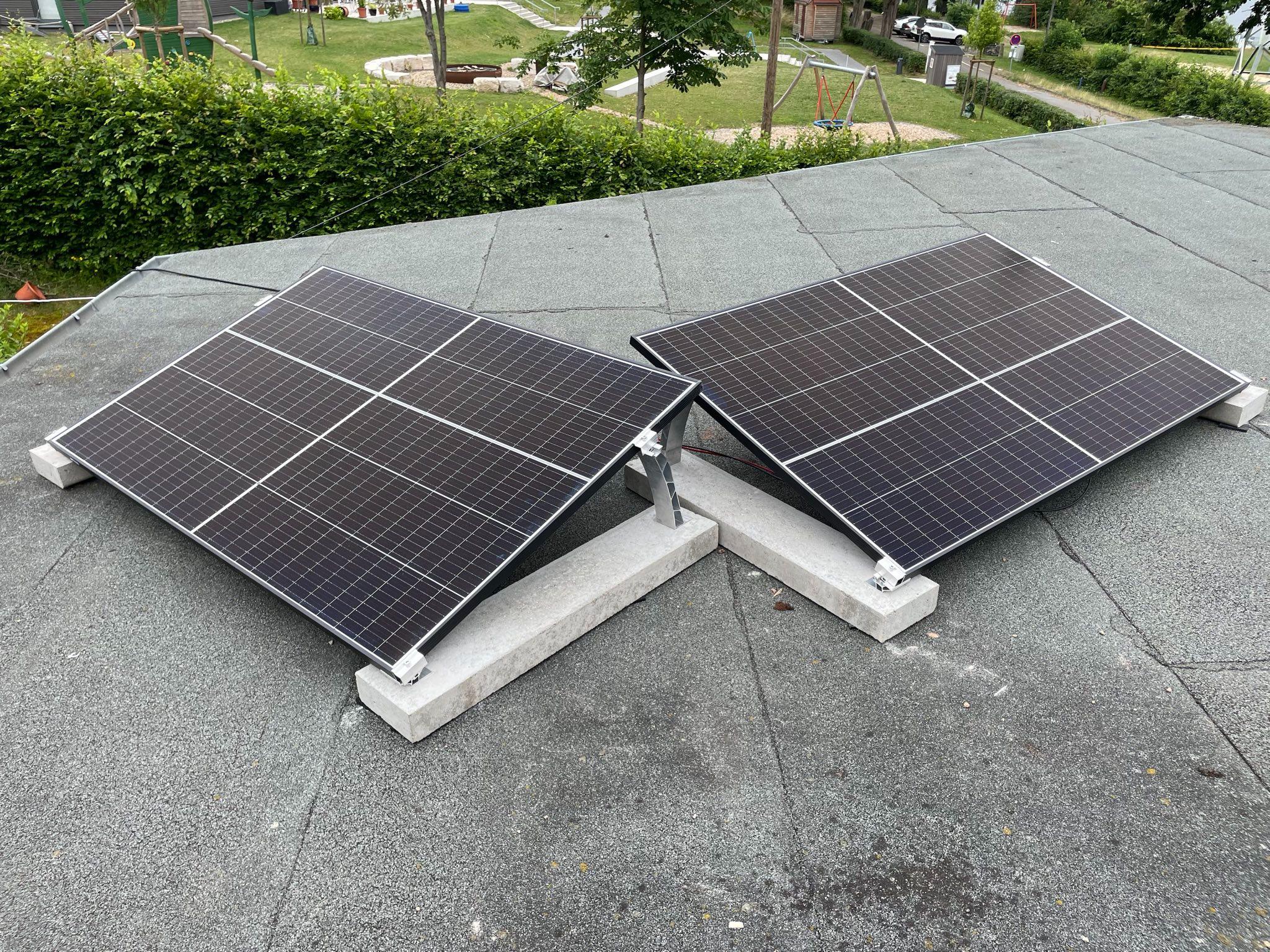 2 Solarpanel auf einem Flachdach, leicht aufgeständert und an Randsteinen befestigt.